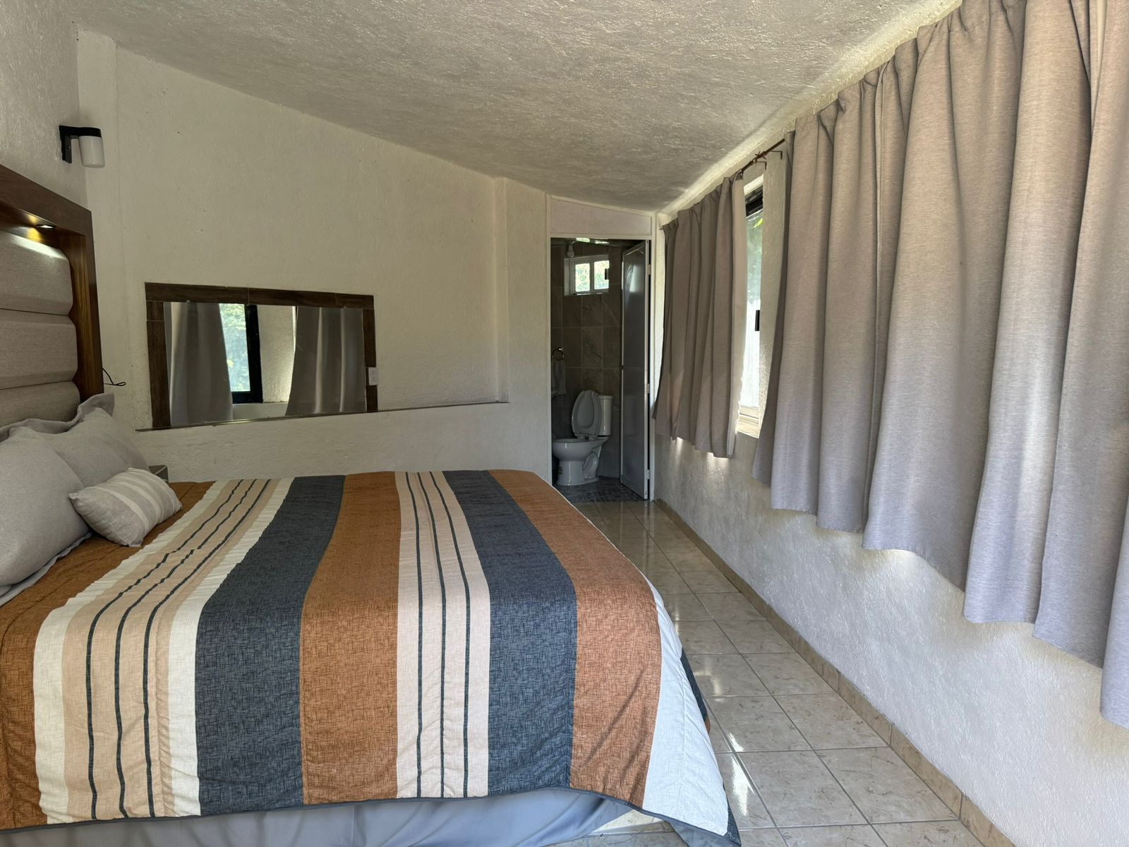A hotel room with a large bed, a bathroom with a toilet and sink, and a window with curtains.
