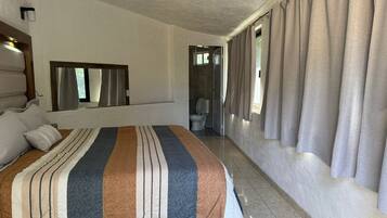 A hotel room with a large bed, a bathroom with a toilet and sink, and a window with curtains.