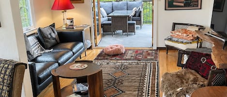 A living room with a sofa, coffee table, and a dining area with a table and chairs. There is a balcony with outdoor furniture.