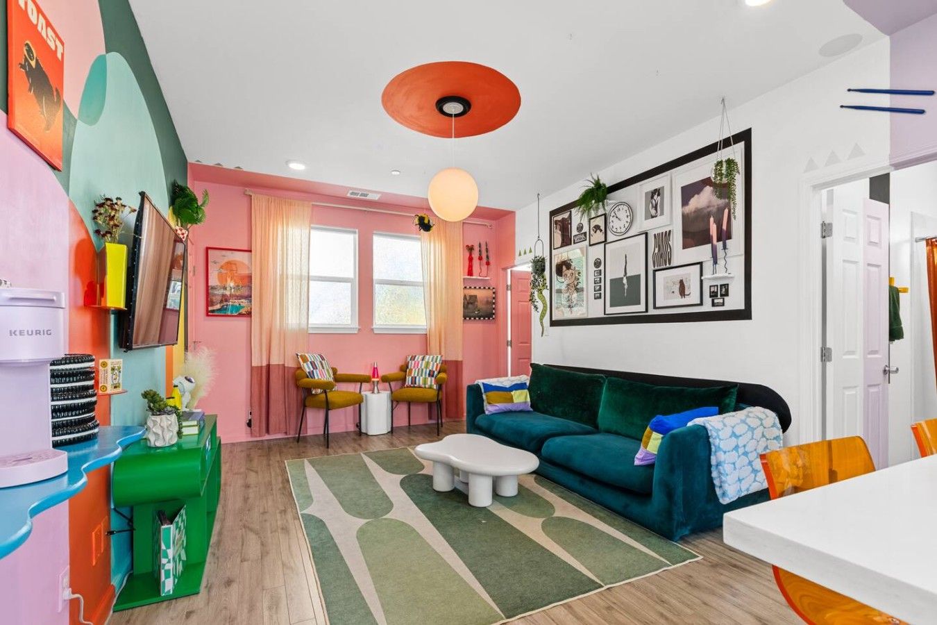 A modern living room with a sofa, chairs, a coffee machine, and a wall with framed pictures.