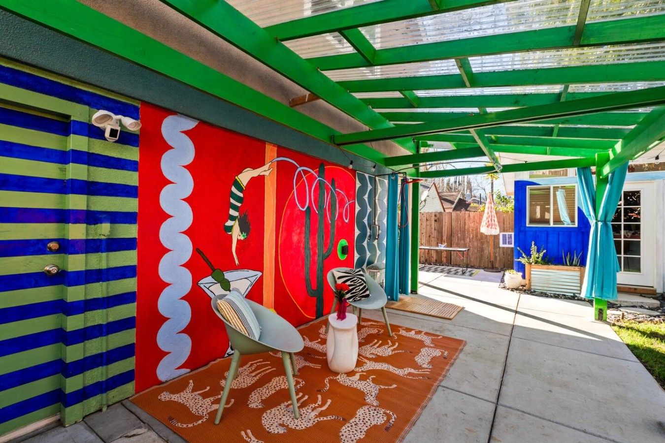 A covered patio area with a colorful mural, a white chair, and a patterned rug.