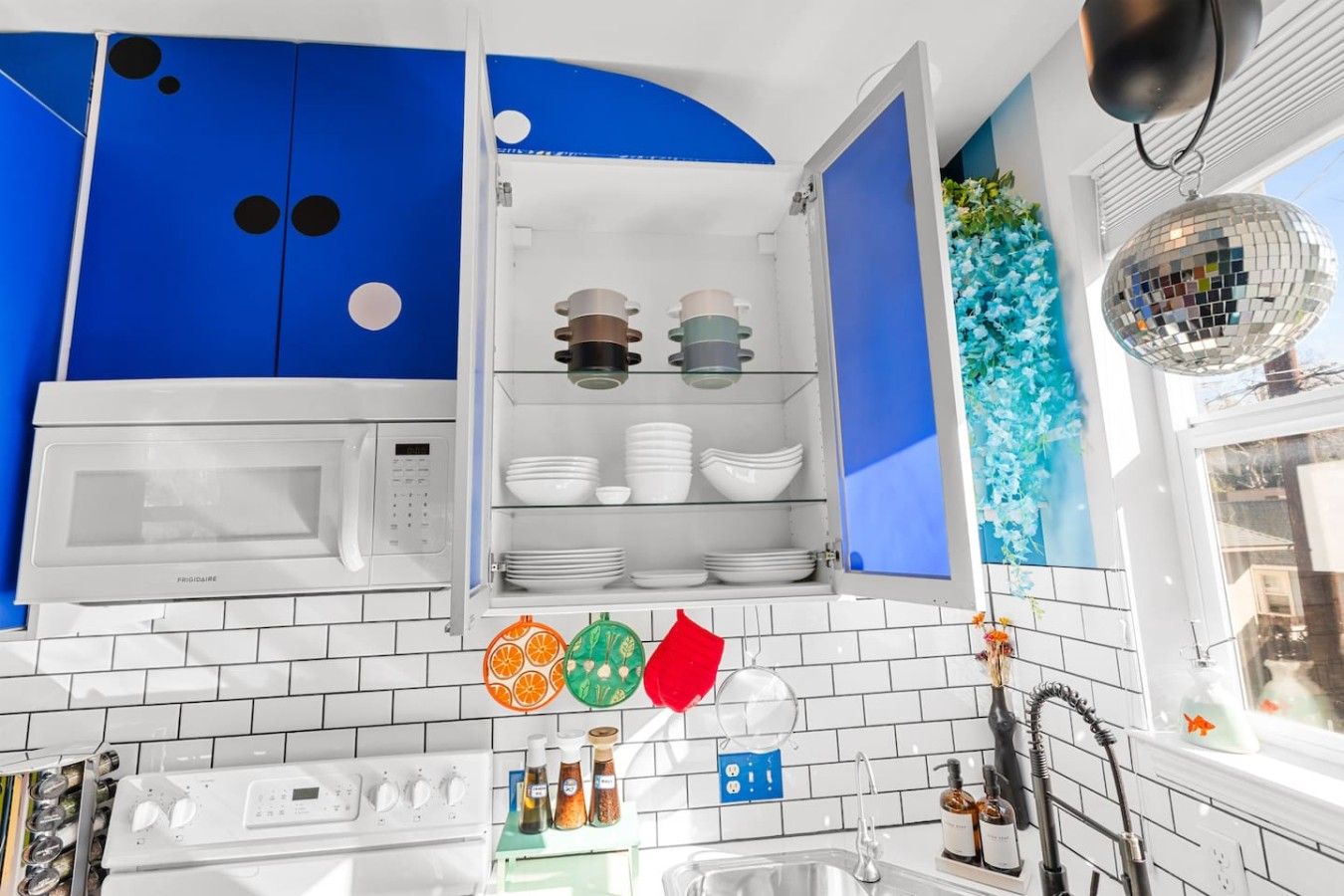 A kitchen with white cabinets, a microwave, a sink, and a window with a view of a blue sky.