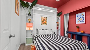 A bedroom with a bed, a wardrobe, a shelf with a plant, and a painting on the wall. - Colorful Retro Pop-Art Bungalow In Midtown (Sacramento)