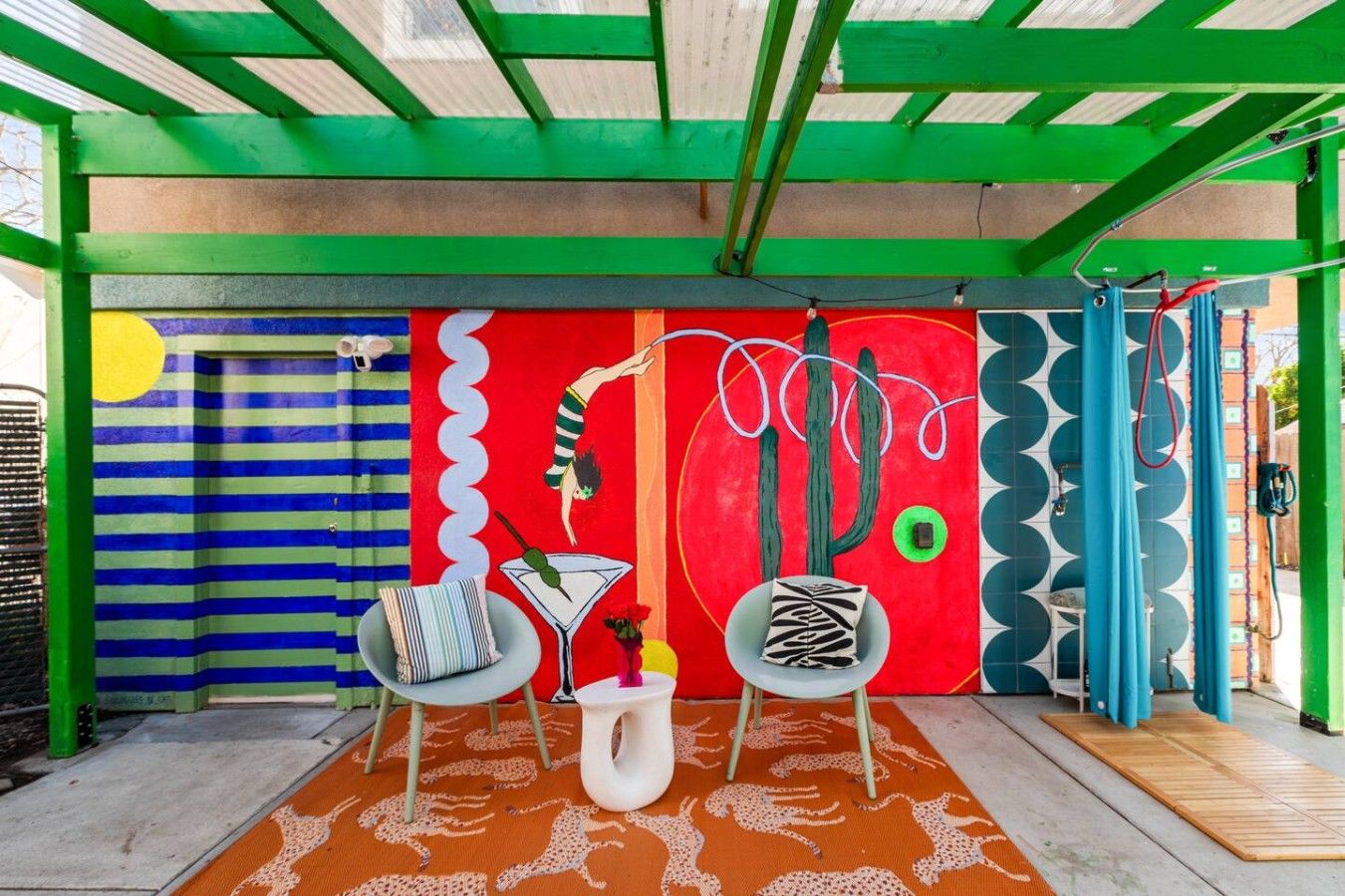 A vibrant outdoor seating area with a colorful mural, two chairs, a small table, and a patterned rug.