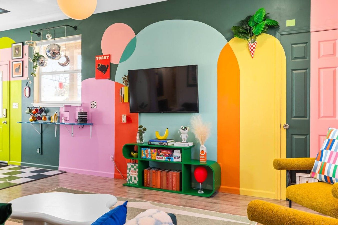 A vibrant living room with a flat-screen TV, colorful walls, a bookshelf, and a yellow armchair.