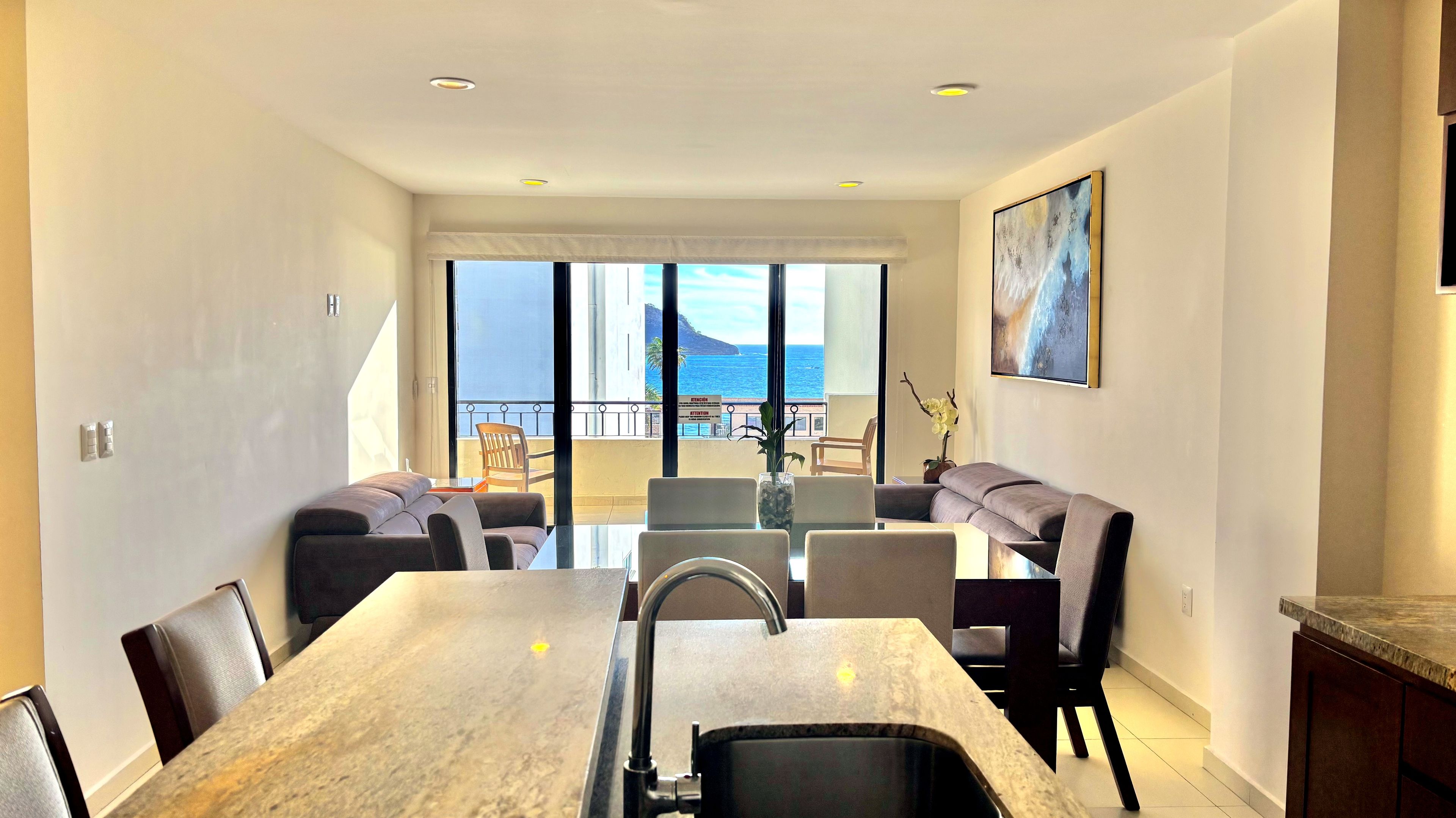 A modern dining area with a marble table, chairs, and a view of the ocean.
