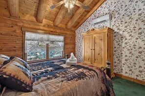 Una habitación de cabaña de madera con una cama grande, un armario de madera y una ventana con vistas a un muro de piedra.