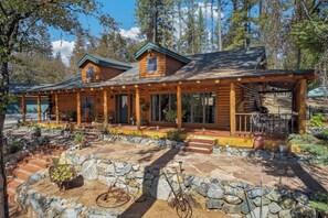 A wooden cabin with a stone patio, multiple windows, and a covered porch area. - Peaceful Log Cabin Getaway on 6 Private Acres (Grass Valley)