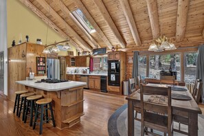 A spacious kitchen with wooden cabinets, a central island with stools, and a dining area with a table and chairs. - Peaceful Log Cabin Getaway on 6 Private Acres (Grass Valley)