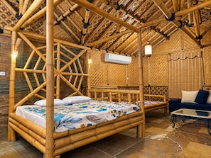 Une chambre dotée d’un lit à baldaquin en bambou, d’un canapé et d’un appareil de climatisation.