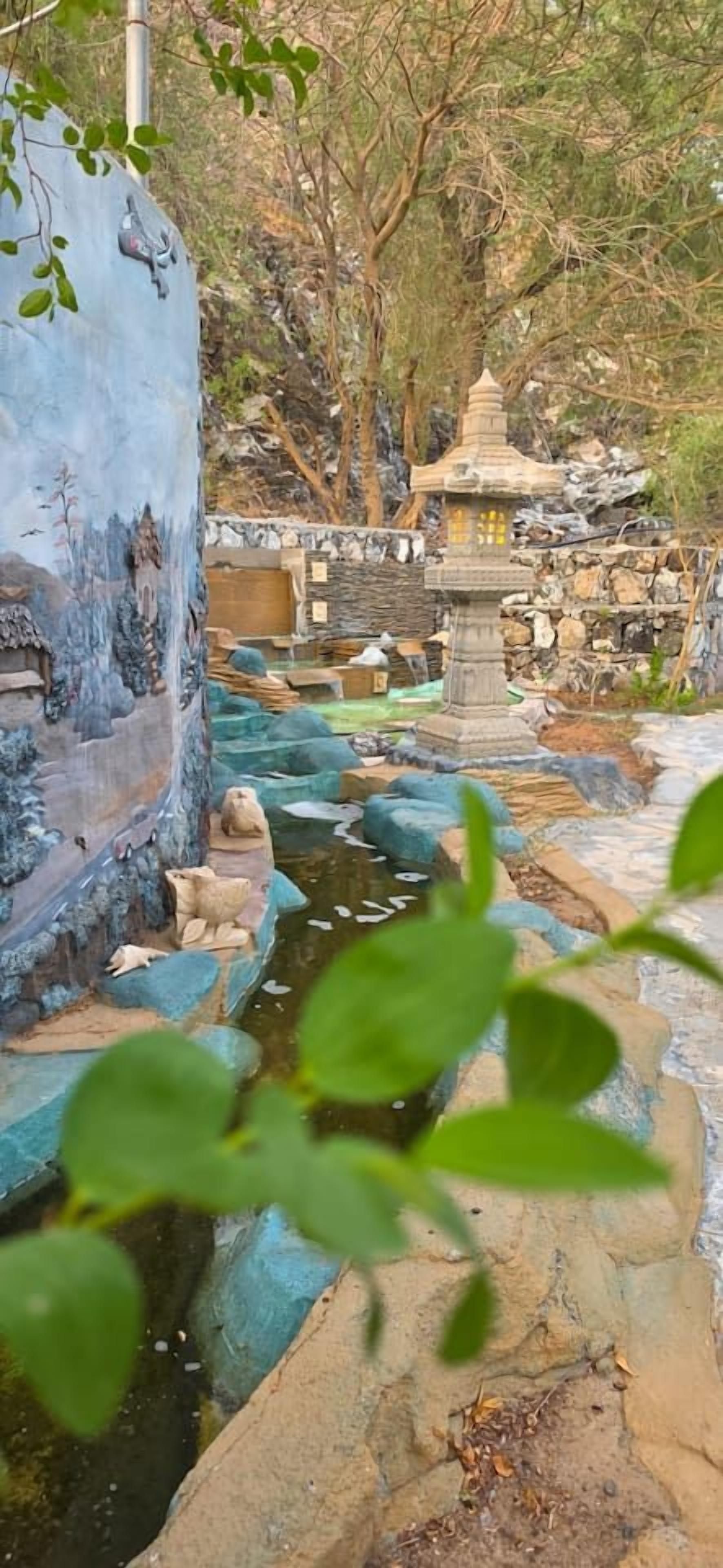 Un jardín tranquilo con un sendero de piedra, un pequeño estanque y una estructura parecida a una pagoda.