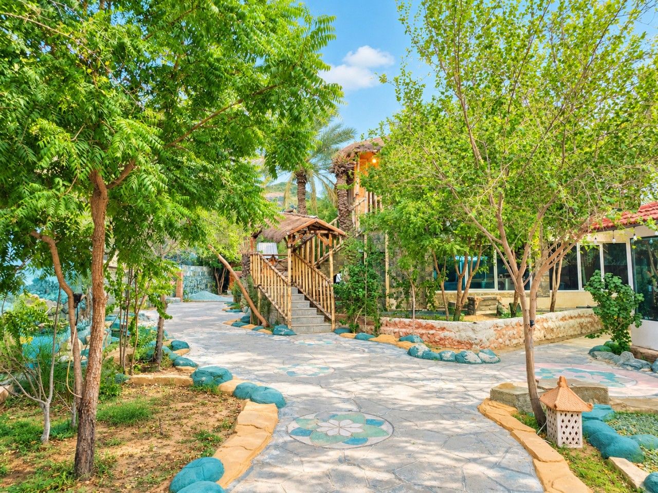 A pathway leading to a wooden staircase surrounded by lush greenery and a stone wall.