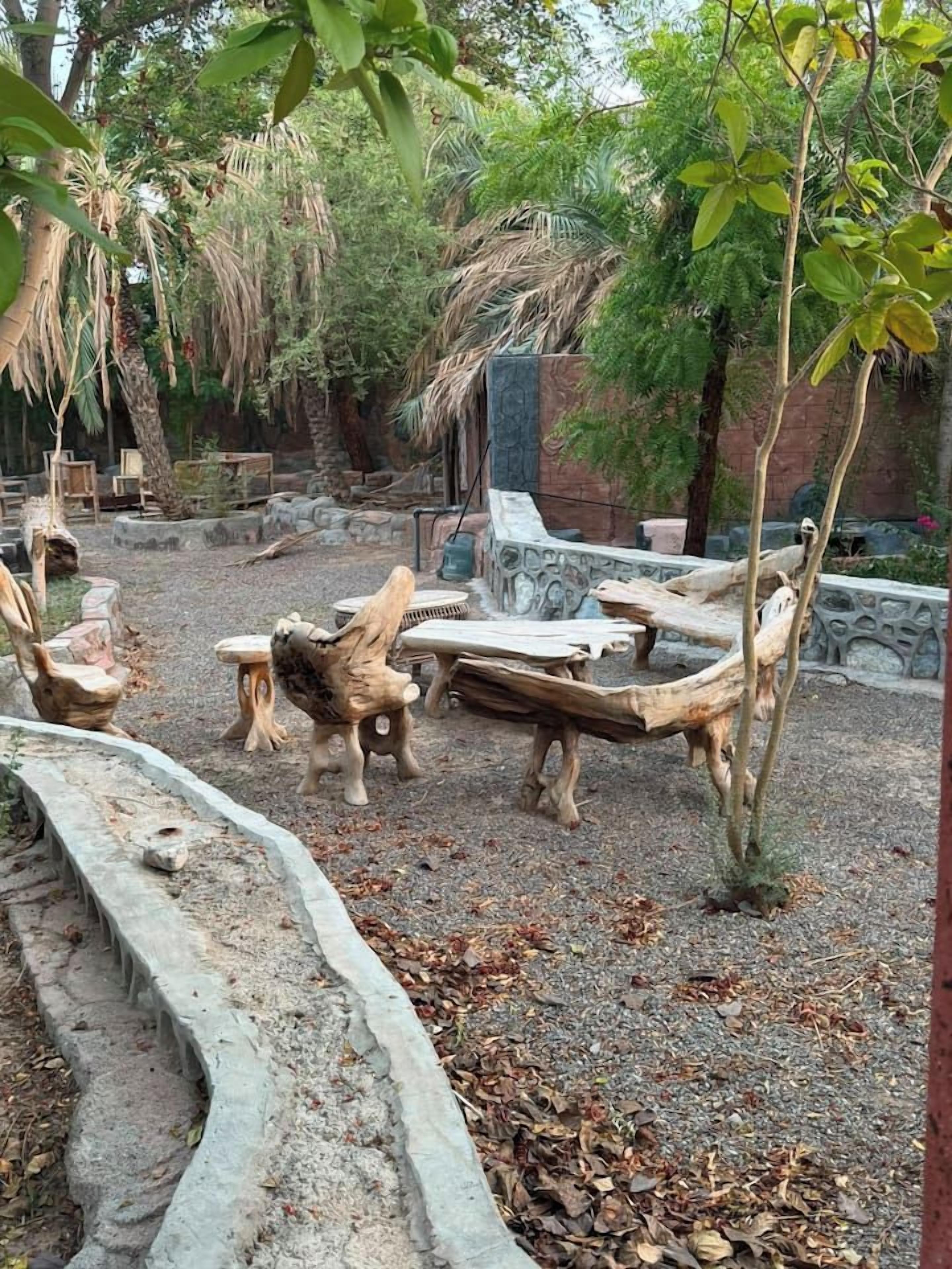 Un área de estar al aire libre de estilo rústico con mobiliario de madera y un muro de piedra al fondo.
