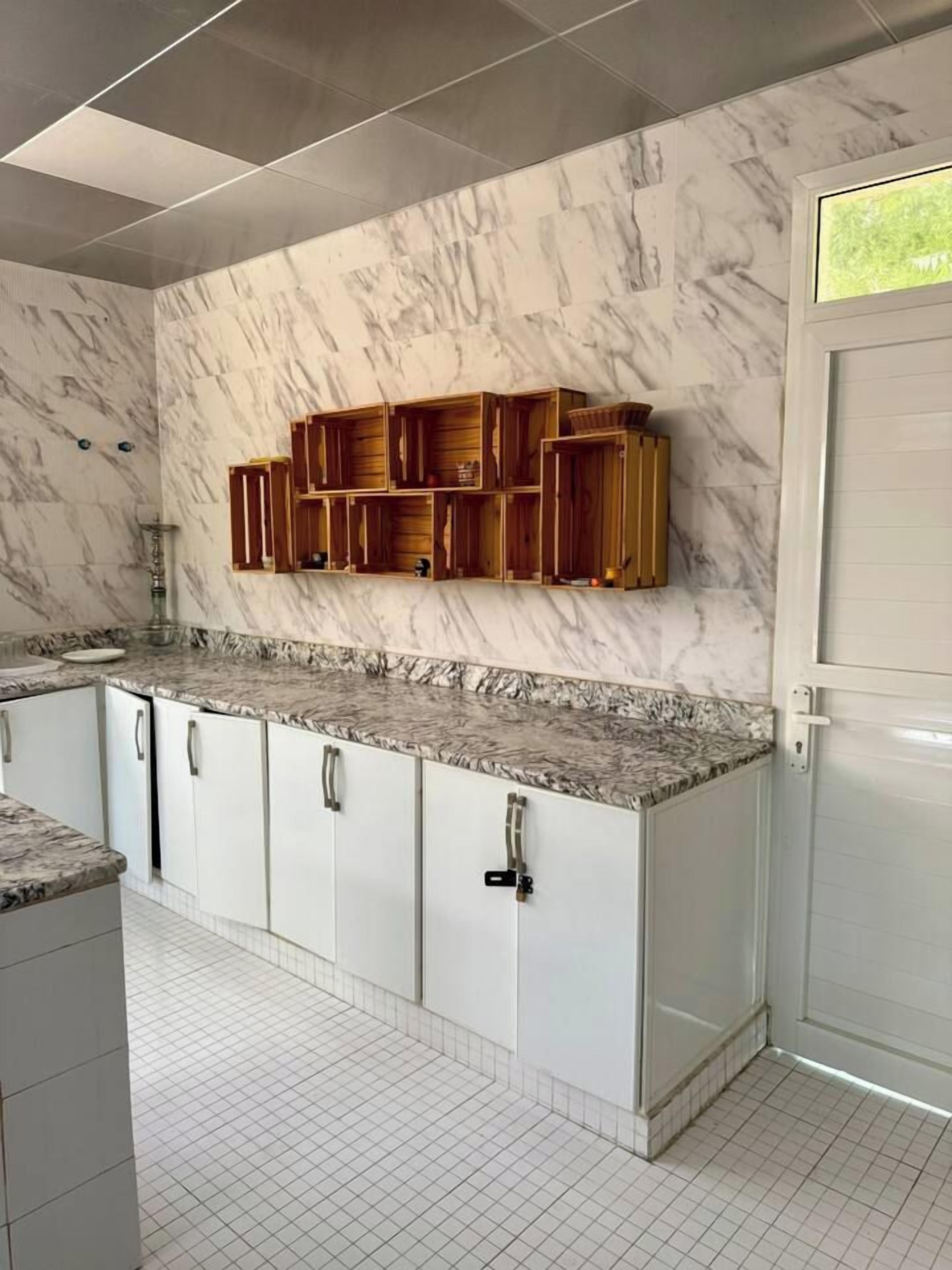 A kitchen with marble countertops, white cabinetry, and wooden shelves above.