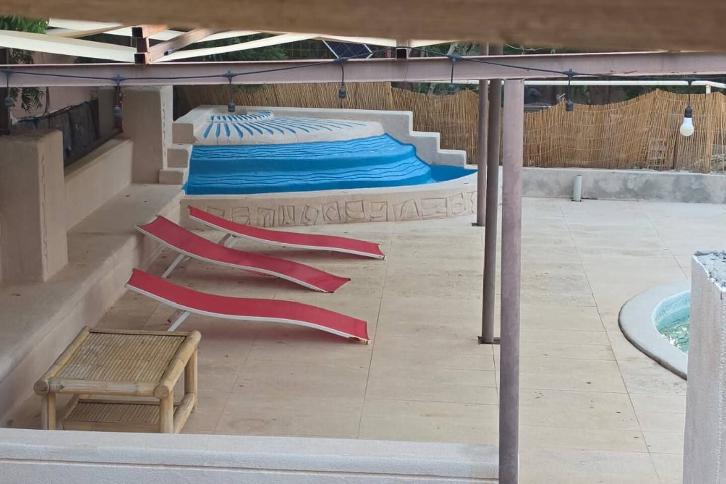 A covered outdoor area with a pool, steps leading to a higher level, and a bamboo fence.