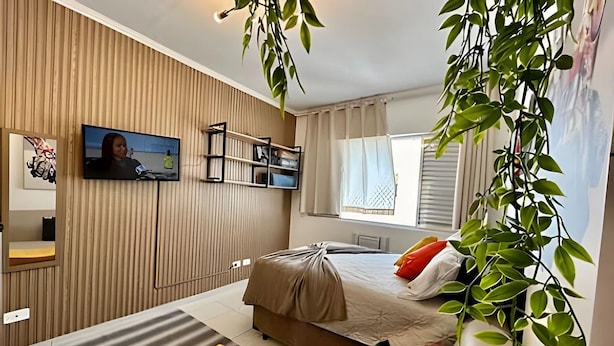 A modern bedroom with a bed, a TV, a shelf, and a window. - SHB - Studio no Gonzaga à Beira Mar (Santos)