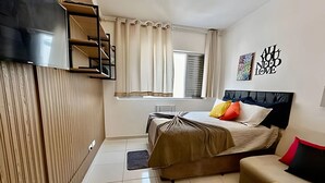 A modern bedroom with a bed, a sofa, a TV, and a window with curtains. - SHB - Studio no Gonzaga à Beira Mar (Santos)