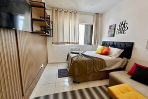 A modern bedroom with a bed, a sofa, a TV, and a window with curtains. - SHB - Studio no Gonzaga à Beira Mar (Santos)