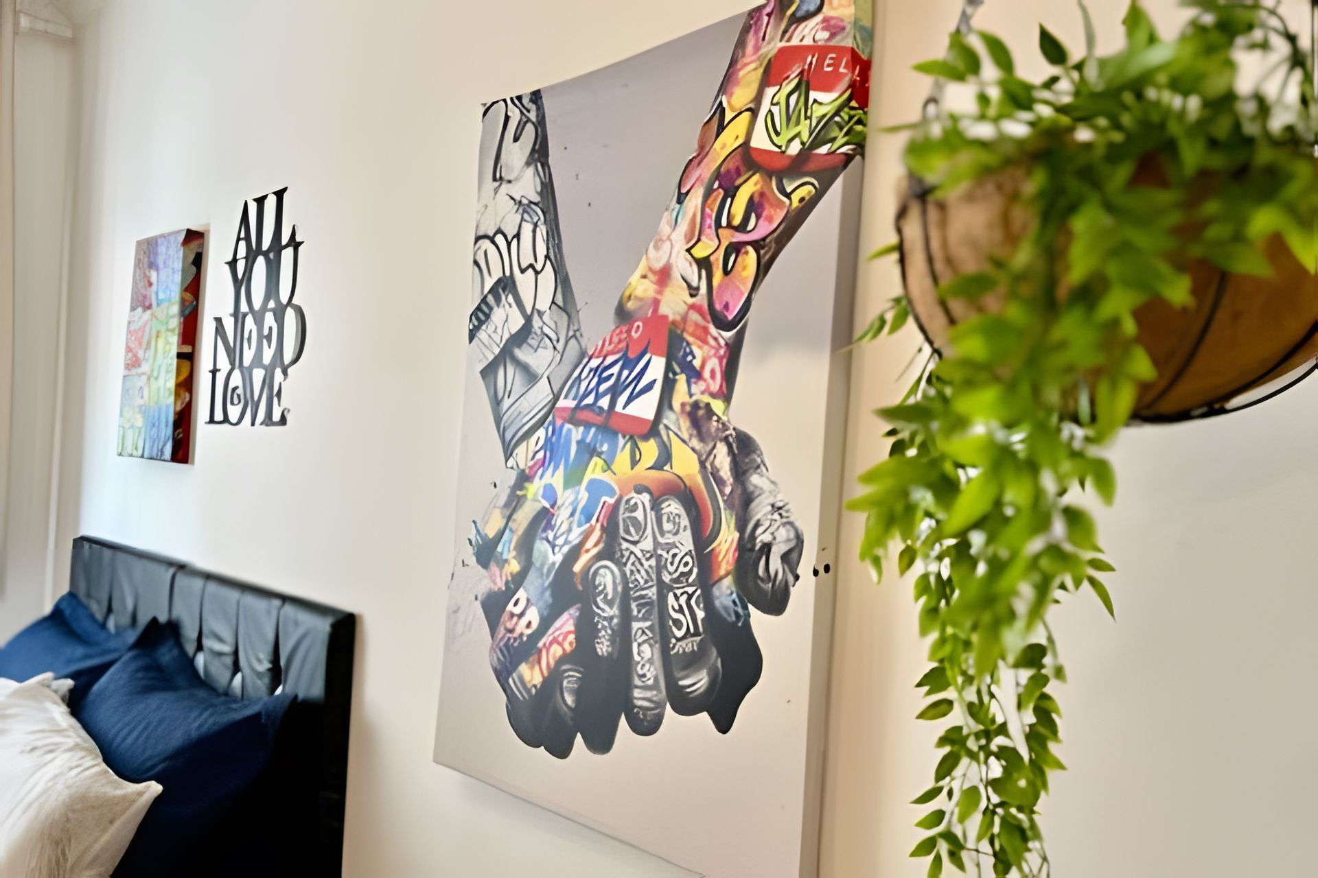 A room with a bed, a wall with a colorful graffiti-style artwork, and a hanging plant.