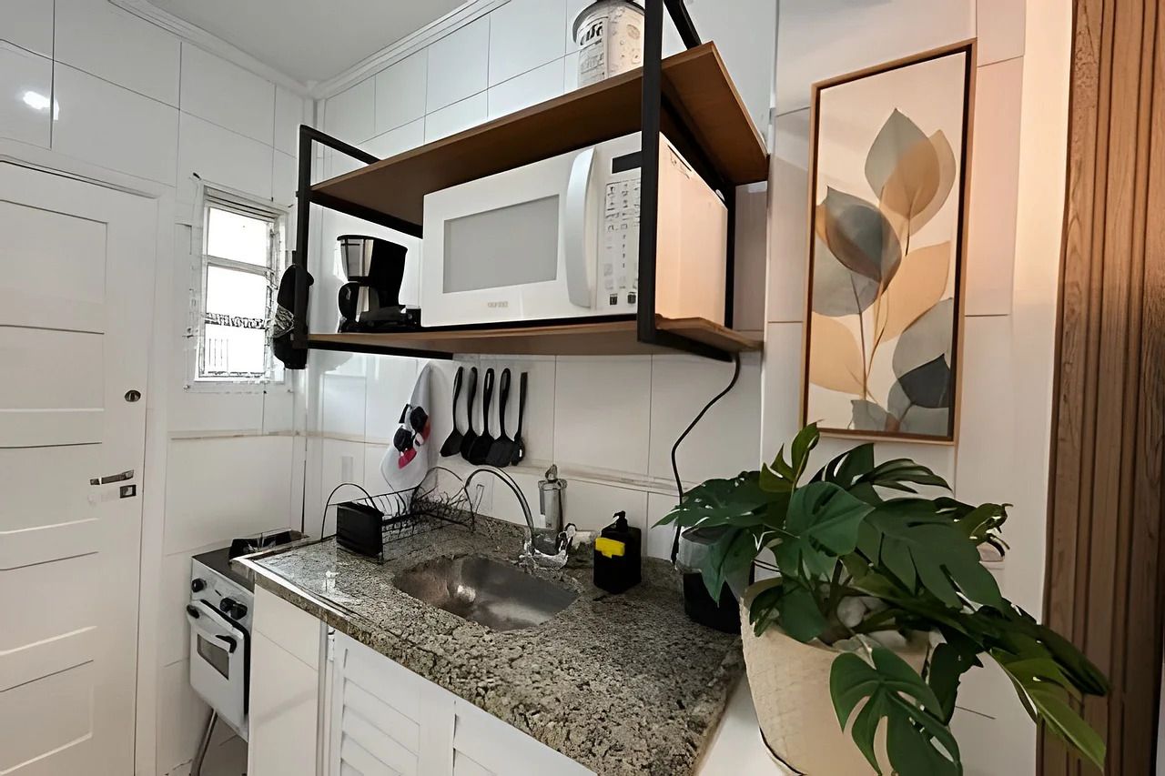 Una cocina con armarios blancos, encimera de granito, microondas empotrado, cafetera y una planta en maceta.