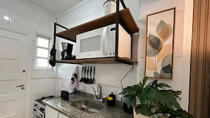 A kitchen with white cabinets, a granite countertop, a built-in microwave, a coffee maker, and a potted plant. - SHB - Studio no Gonzaga à Beira Mar (Santos)