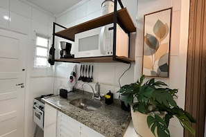 A kitchen with white cabinets, a granite countertop, a built-in microwave, a coffee maker, and a potted plant. - SHB - Studio no Gonzaga à Beira Mar (Santos)