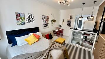 A modern bedroom with a bed, bedside tables, a desk, and a kitchenette.