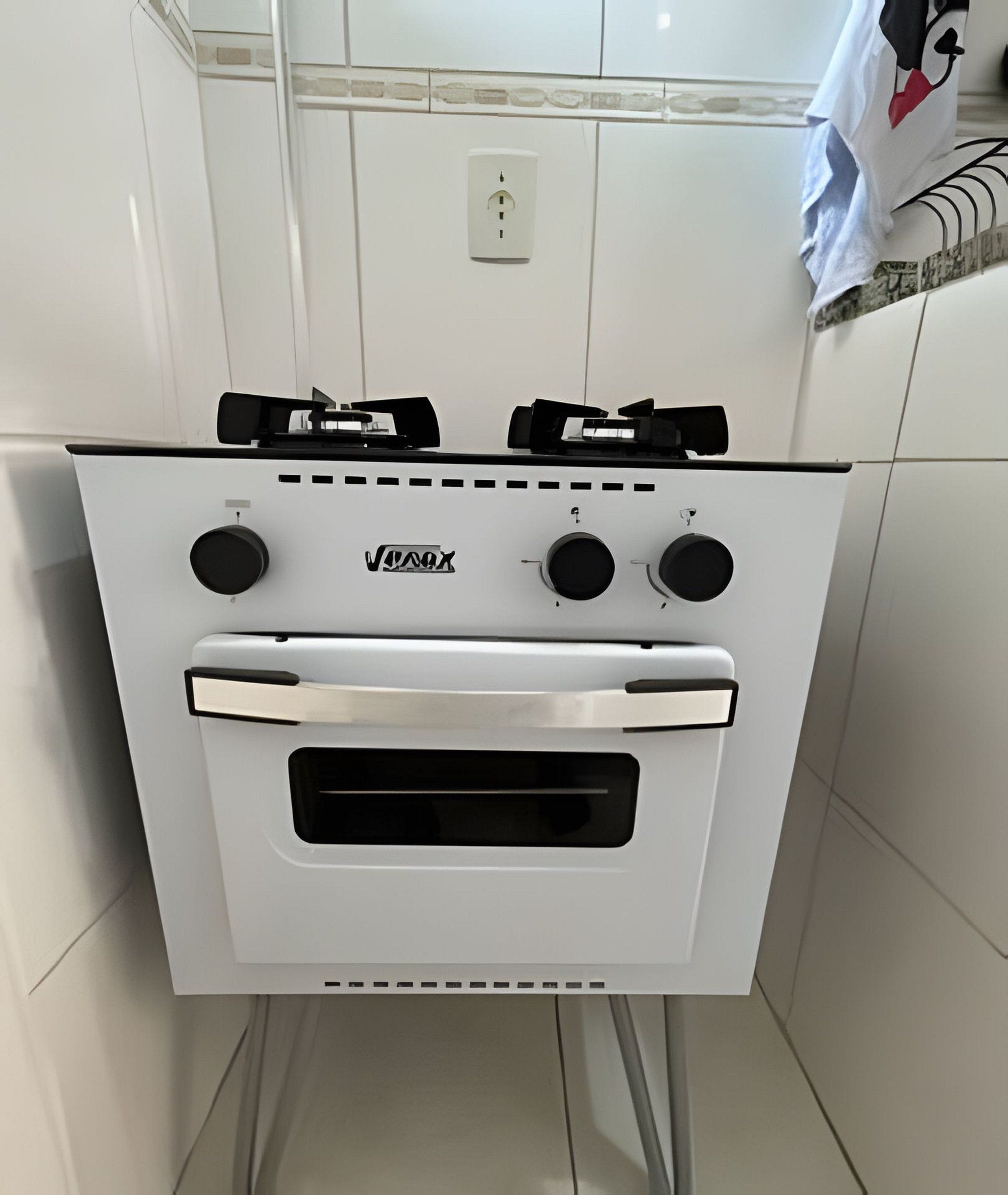 A white kitchen with a stove and oven, a tiled backsplash, and a power outlet above the stove.