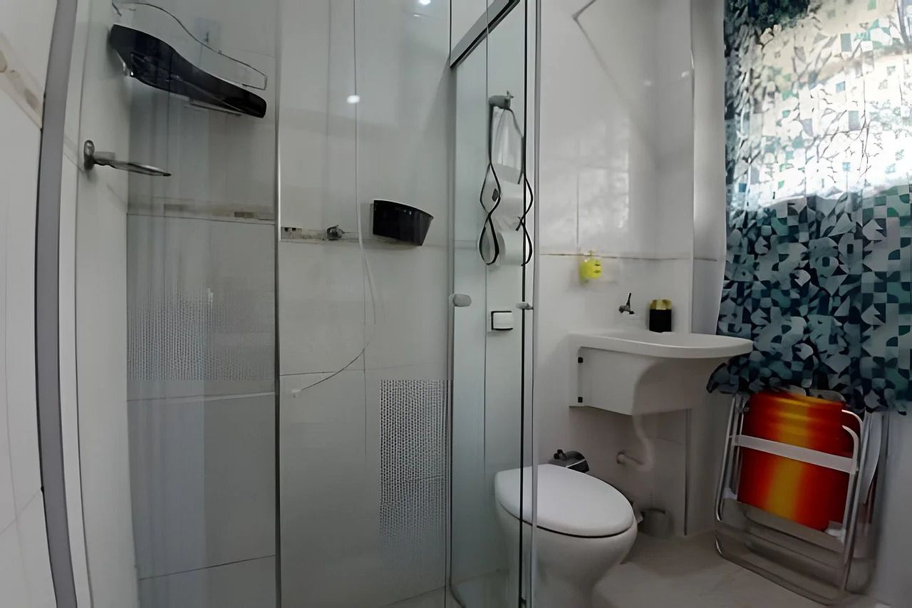 Un baño moderno con cabina de ducha de vidrio, inodoro blanco y lavamanos con cortina estampada.