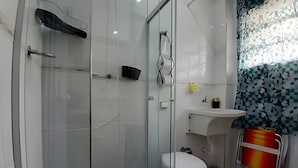 A modern bathroom with a glass shower enclosure, a white toilet, and a sink with a patterned curtain. - SHB - Studio no Gonzaga à Beira Mar (Santos)