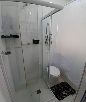 Une salle de bain moderne avec une douche à parois de verre, des toilettes et une petite étagère.
