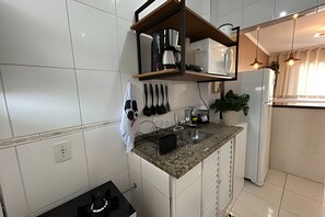 A modern kitchen with white tiles, a granite countertop, a built-in oven, a coffee maker, and hanging utensils. - SHB - Studio no Gonzaga à Beira Mar (Santos)