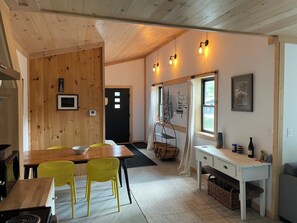 A cozy kitchen with wooden walls, a dining table with chairs, a white desk, and a window with a view.