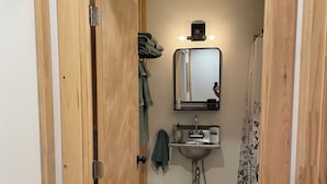 Un corridoio stretto che conduce a un bagno con lavandino, specchio e un piccolo ripiano con articoli da toilette.