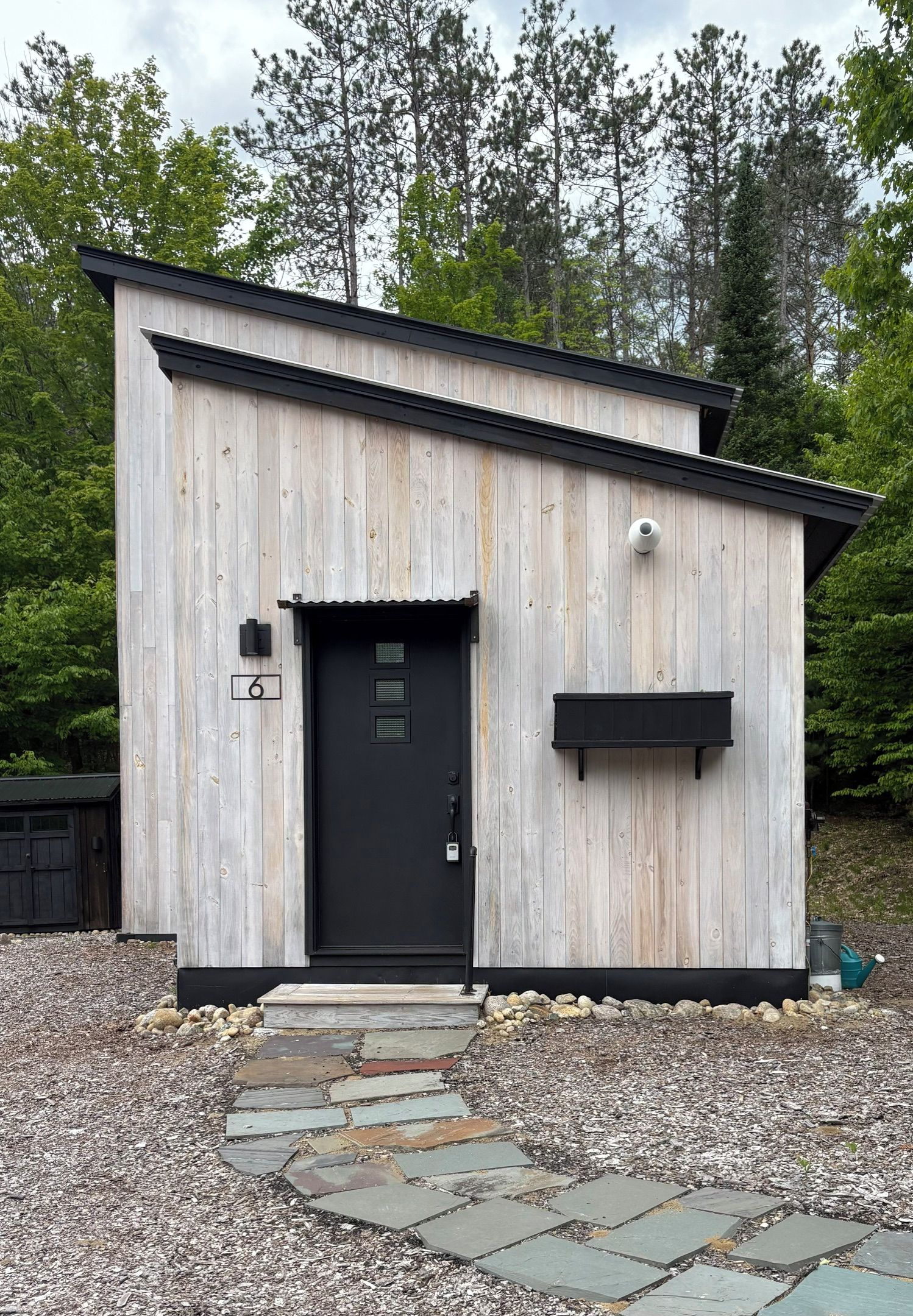 A small, single-story wooden building with a black door and a small black mailbox.
