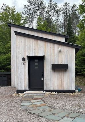A small, single-story wooden building with a black door and a small black mailbox.