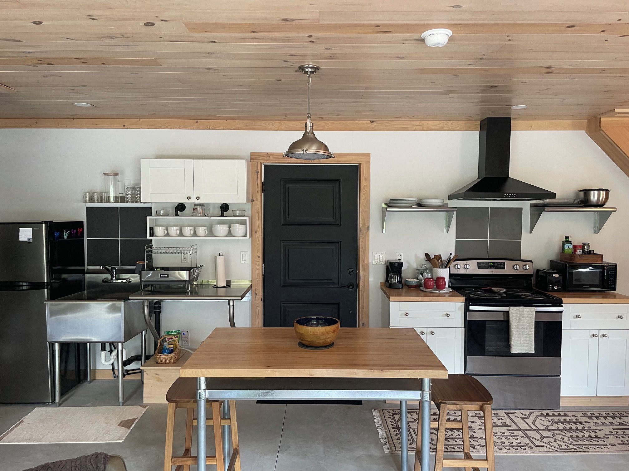 A modern kitchen with a central island, stainless steel appliances, and a black door.