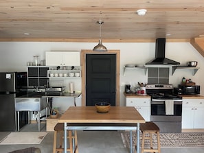 A modern kitchen with a central island, stainless steel appliances, and a black door.