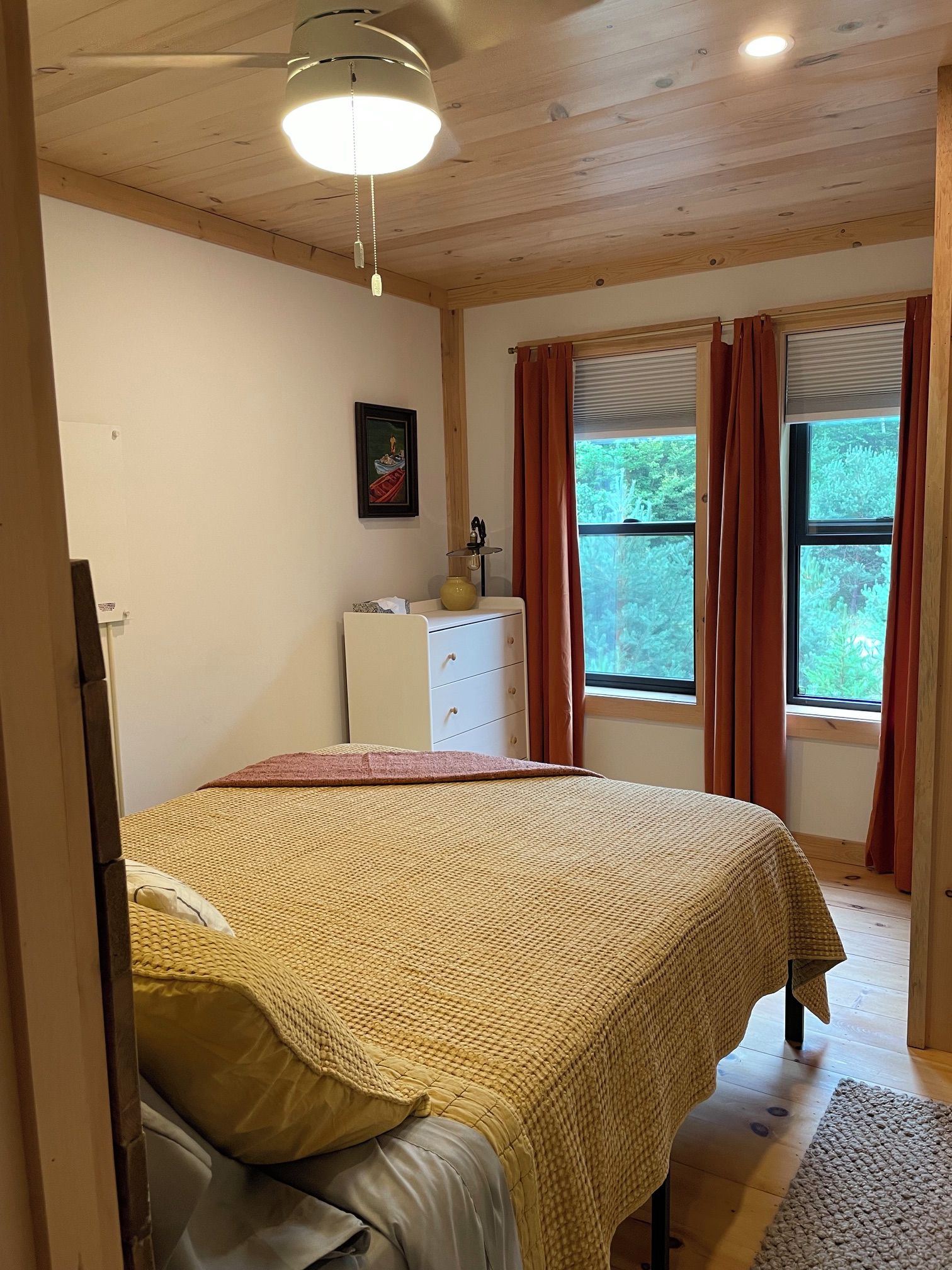 A bedroom with a bed, a dresser, a window with curtains, and a ceiling light.