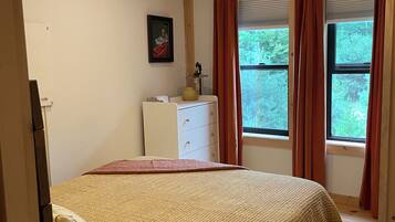 A bedroom with a bed, a dresser, a window with curtains, and a ceiling light.