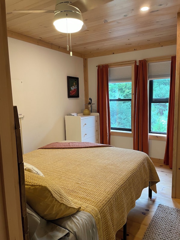 A bedroom with a bed, a dresser, a window with curtains, and a ceiling light.