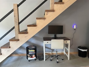 A staircase with wooden steps and black railings, a desk with a computer and chair, a bookshelf, and a trash can.