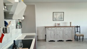 A kitchen with white cabinets, a wooden chair, and a framed picture on the wall. - Zefiro Apartment in Alghero. The perfect place to visit the Coral Riviera (Fertilia)