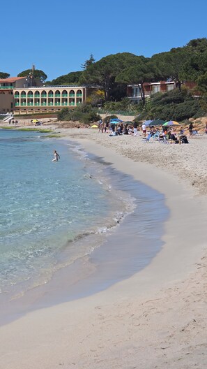A beach with clear water, people sunbathing, and buildings in the background. - Zefiro Apartment in Alghero. The perfect place to visit the Coral Riviera (Fertilia)