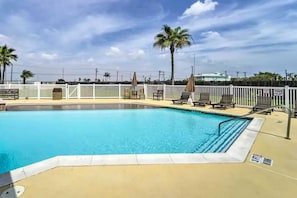 A swimming pool with a white fence, lounge chairs, and palm trees. - Isla Bella - 2BR Beach Condo with Pools & Hot Tubs (South Padre Island)