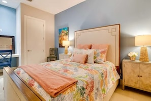 A bedroom with a bed, bedside tables, a chair, a door, and a painting on the wall. - Isla Bella - 2BR Beach Condo with Pools & Hot Tubs (South Padre Island)