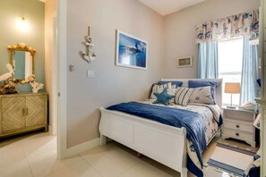 Une chambre à coucher comprenant un lit, une table de chevet, une commode, un miroir et une fenêtre avec des rideaux.