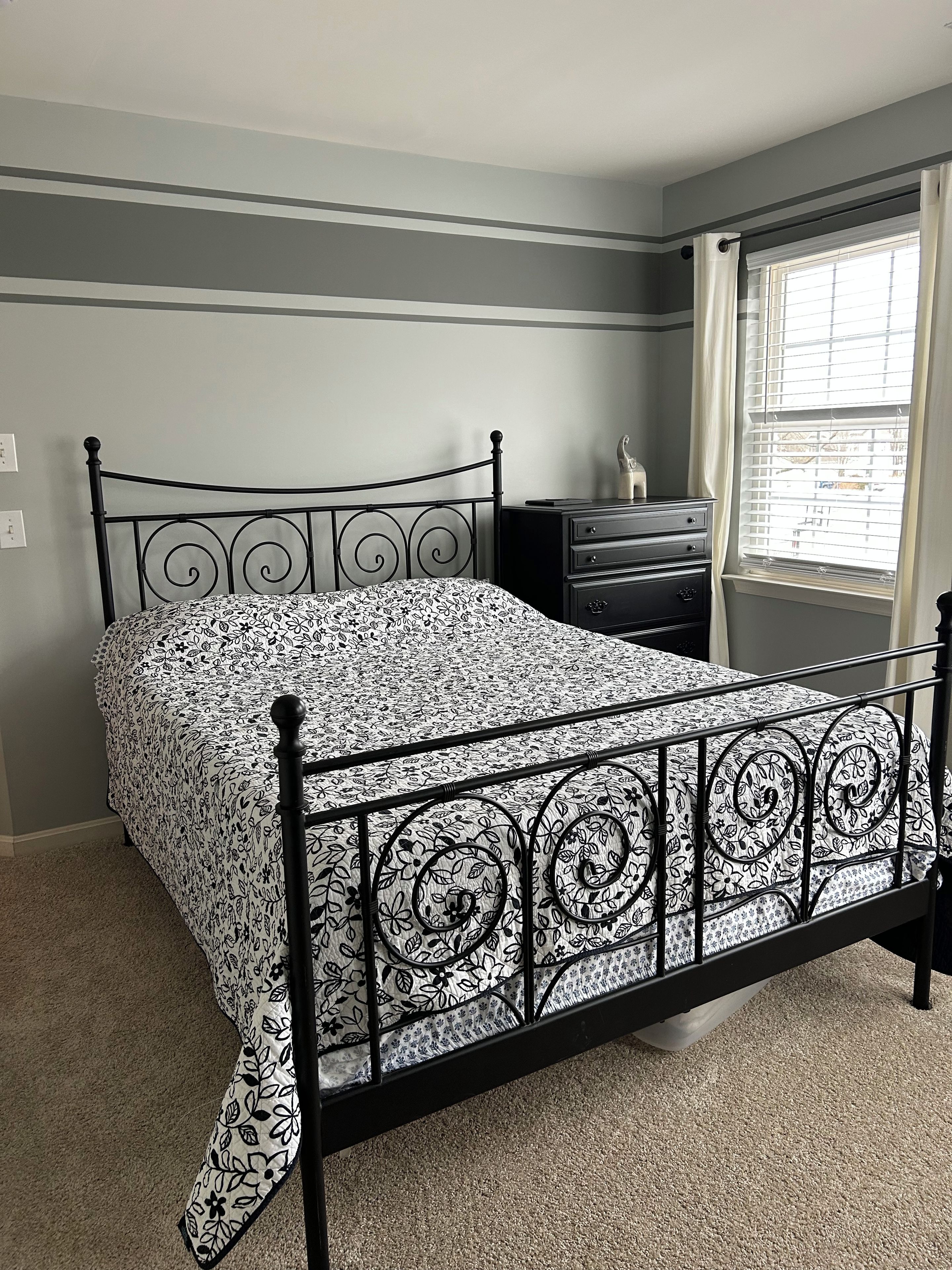 A bedroom with a metal bed frame, a bedside table, and a window with blinds.