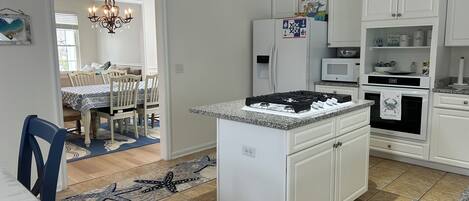 Una cocina con armarios blancos, una isla central con estufa, refrigerador y microondas. Hay un comedor con mesa y sillas.