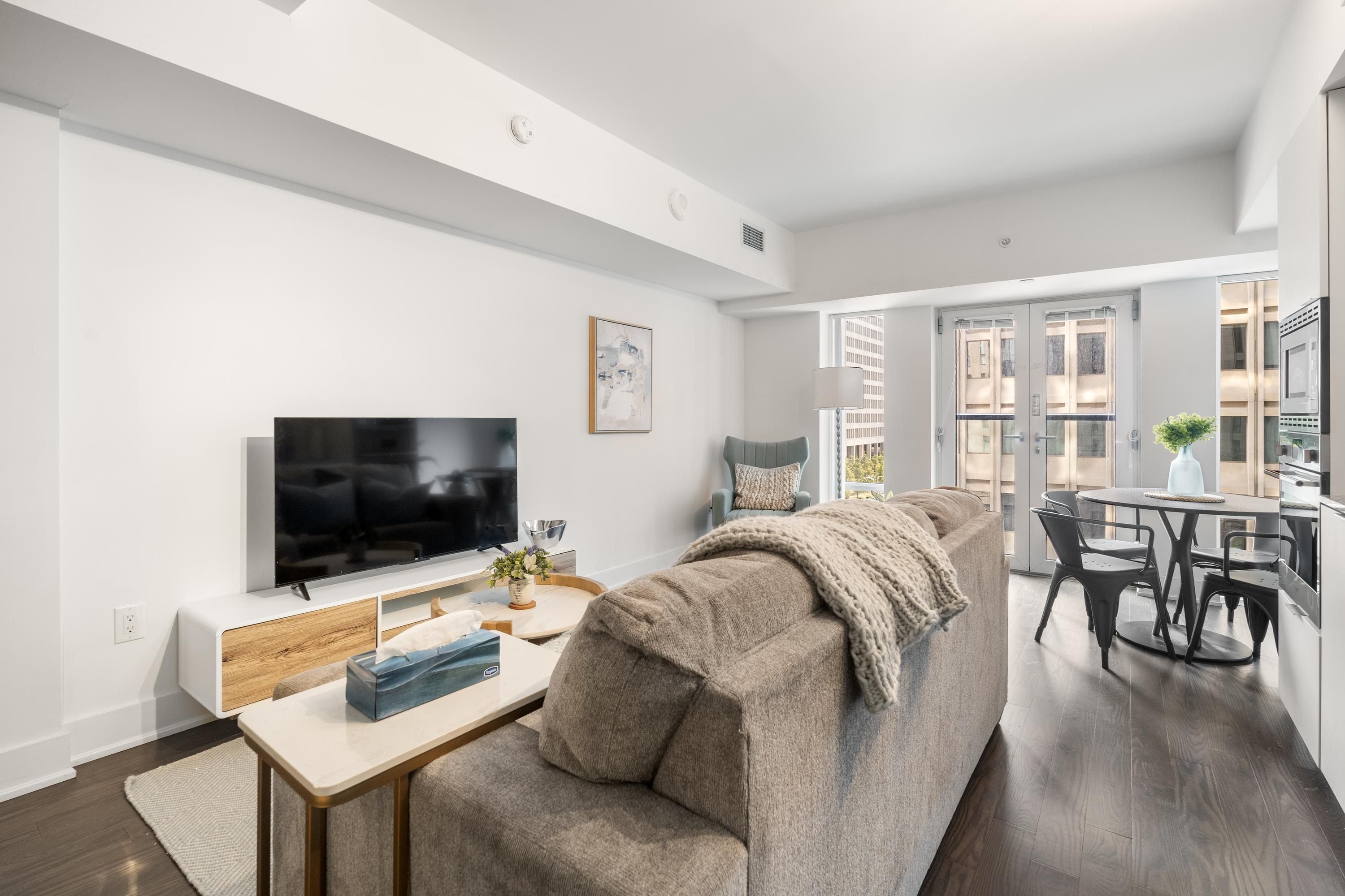 Een moderne woonkamer met een grote flatscreen televisie, een bank, een salontafel en een eethoek met een ronde tafel en stoelen.